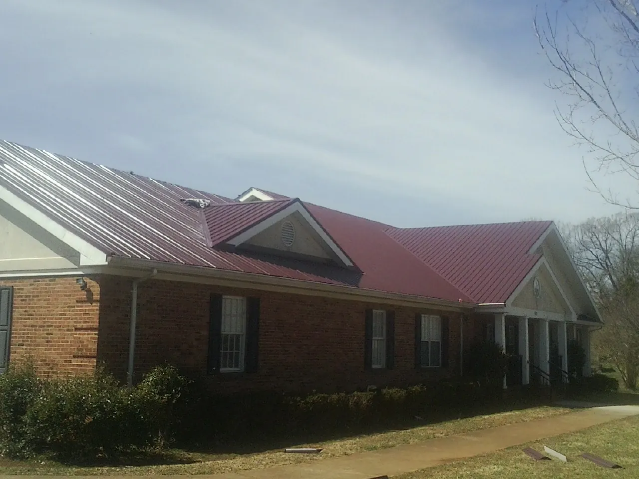 Red metal roof with gabled entries on a long brick building, from a Hail Damage Roof Repair job in Uhrichsville