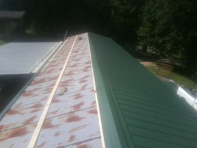 Old rusted panels beside newly installed green metal roofing — Wind Damage Roof Repair by Roofing Brothers in Uhrichsville
