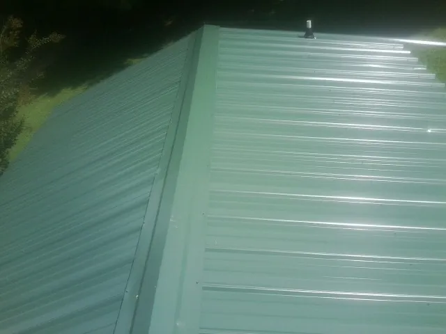 New green metal panels meeting at the ridge of a roof — Flat Roof Repair work by our crew in Uhrichsville
