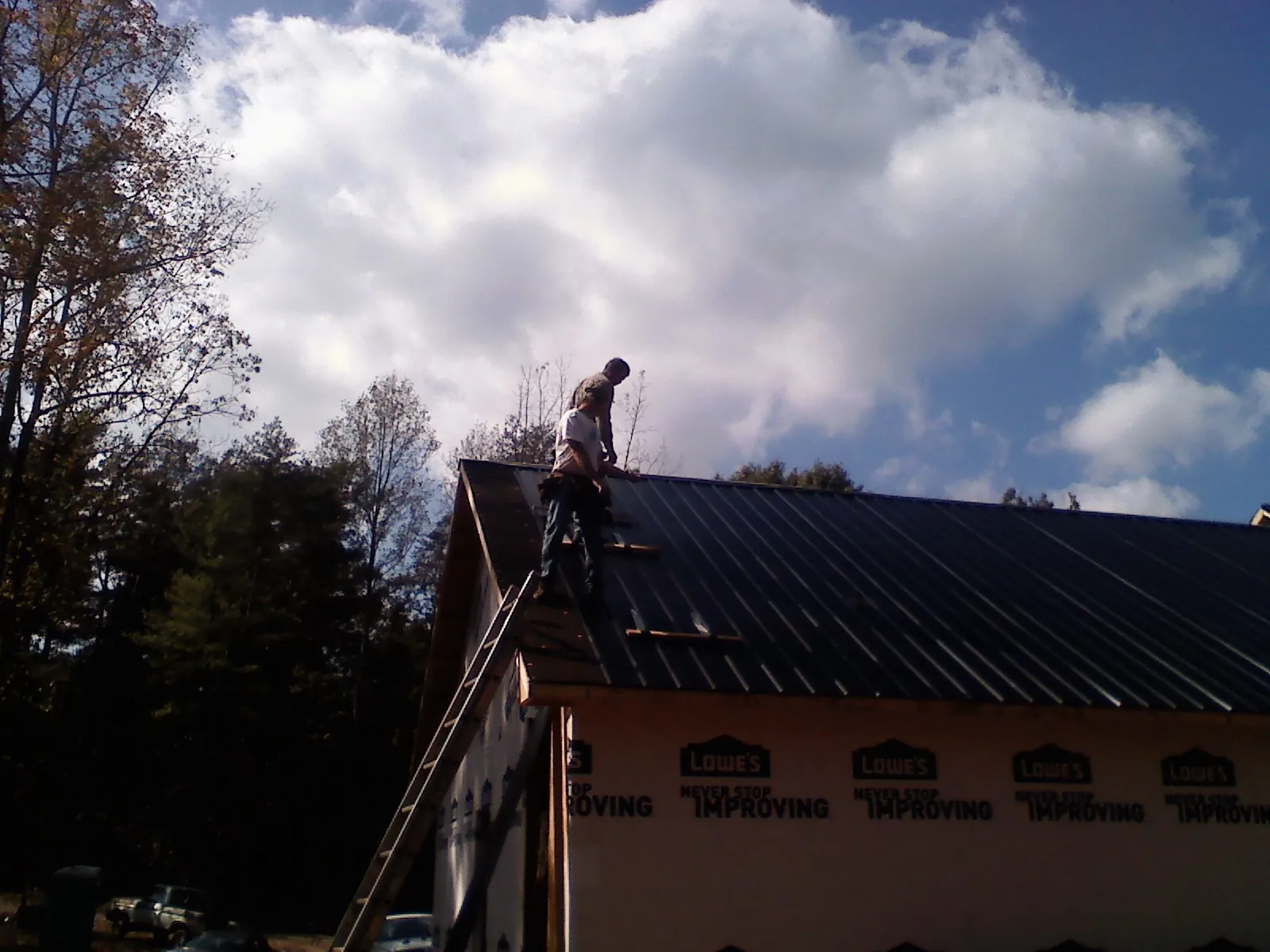 Roofer fastening dark metal panels high against a cloudy sky, from a Roof Inspection job in Uhrichsville
