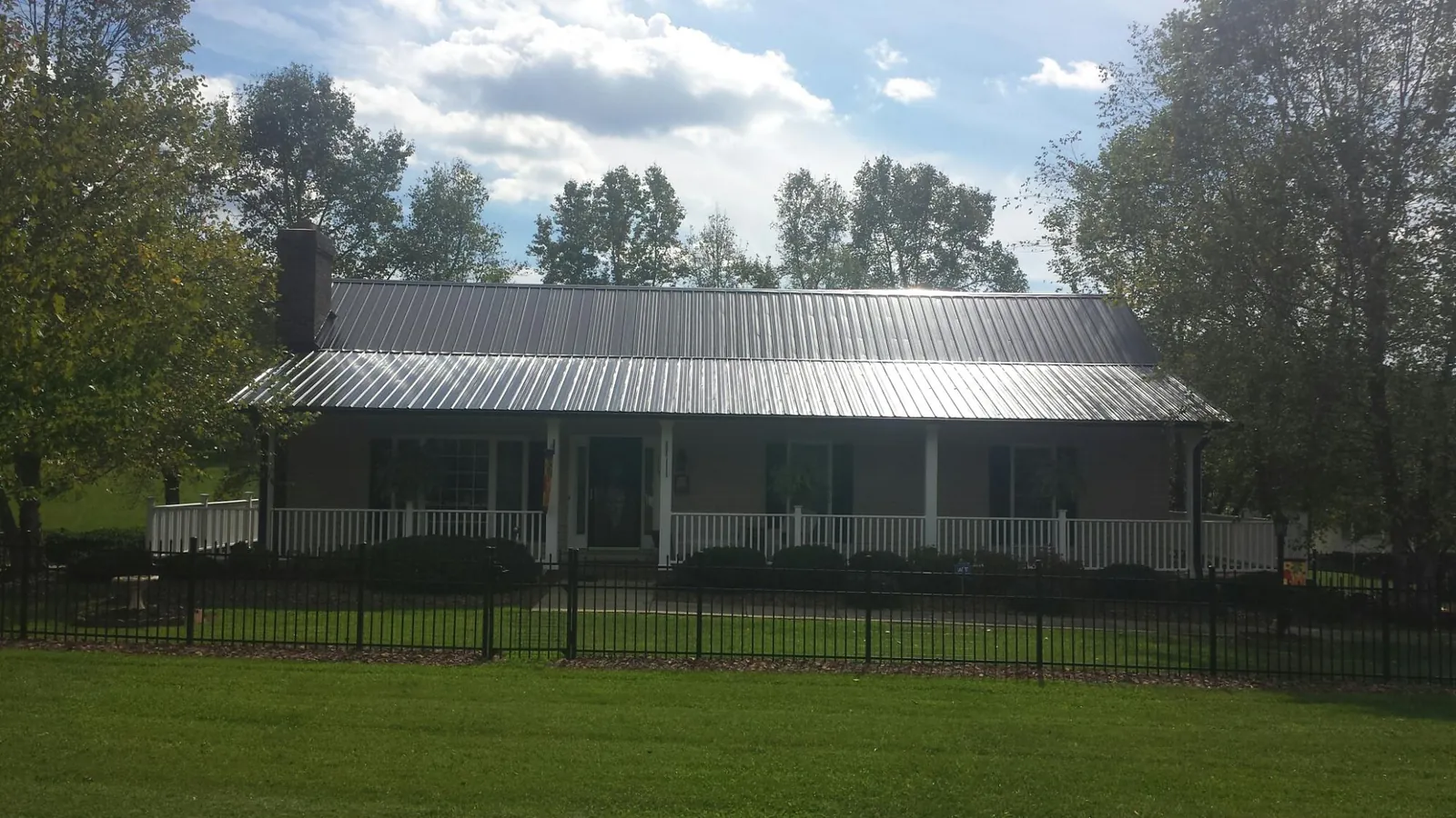 Gray metal roof on a brick ranch with a full width front porch — Gutter Guard Installation work by our crew in Uhrichsville