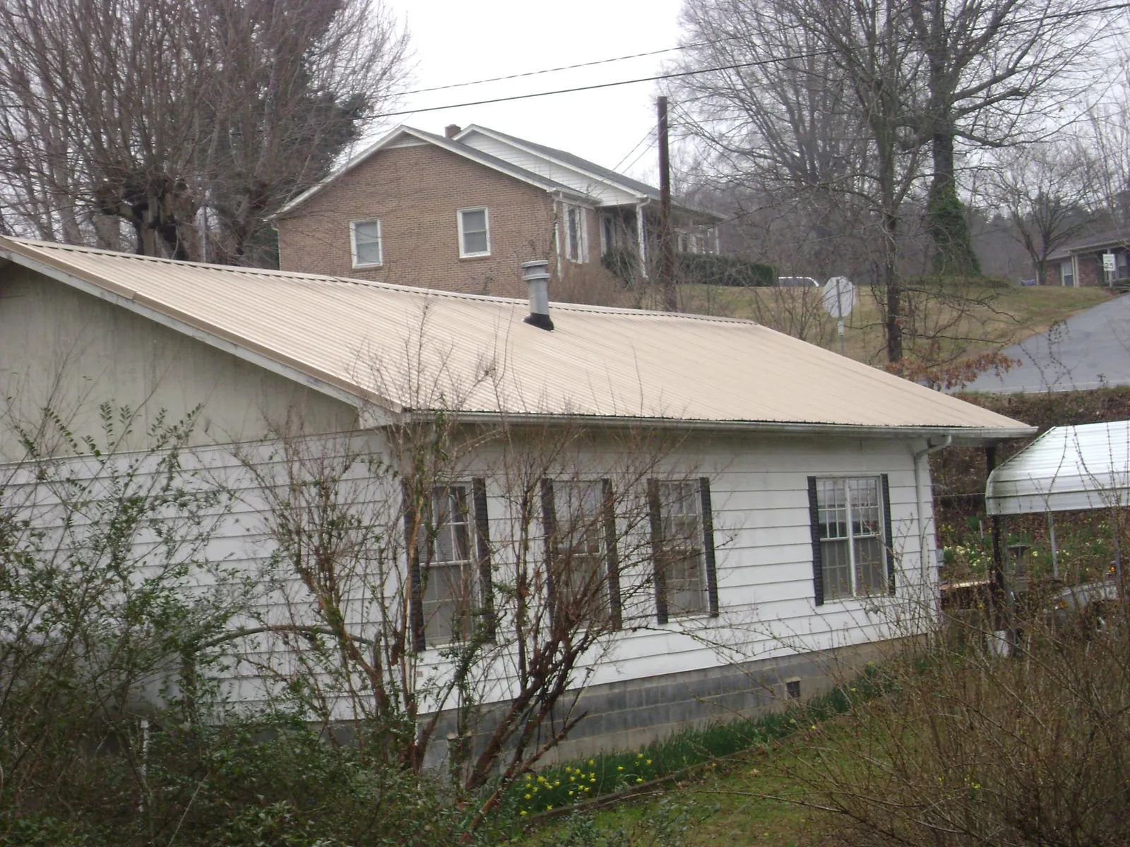 Tan metal roof on a white sided house set into a hillside — Commercial Roofing by Roofing Brothers in Uhrichsville