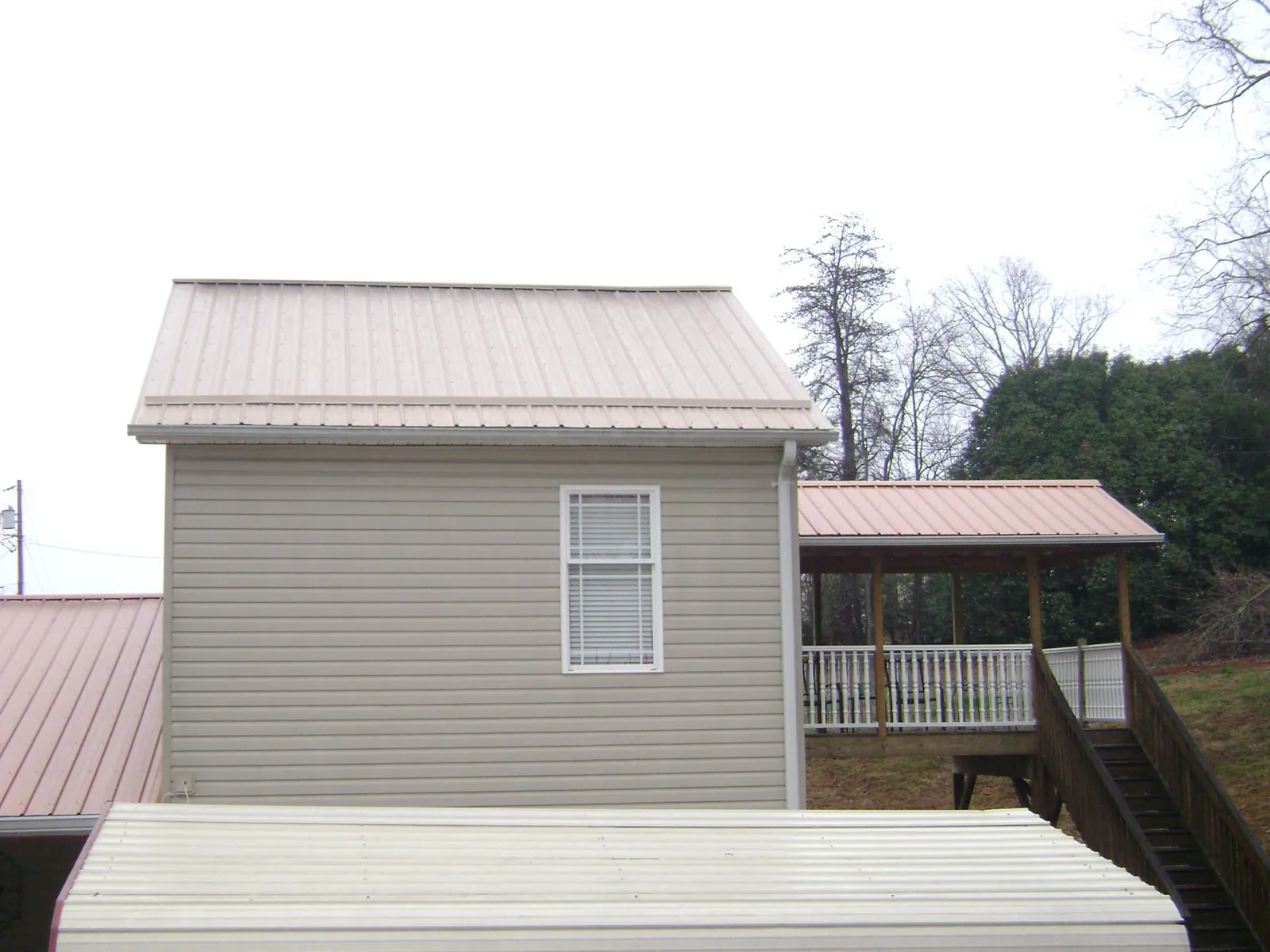 Tan metal roofs on a two story addition and attached porch, from a Roof Replacement job in Uhrichsville